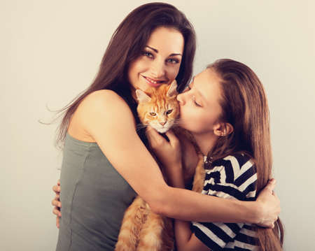 Happy young mother hugging her red maine coon kitten and daughter. Closeup portrait of smiling family. Toned vintage colorの写真素材