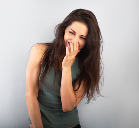 Happy laughing beautiful woman covering the face the hands on blue background and happy looking in green t-shirt. Portrait with empty copy spaceの写真素材