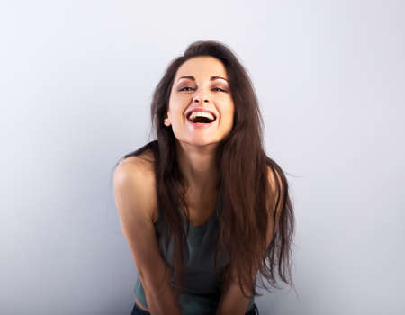 Happy laughing beautiful woman covering the face the hands on blue background and happy looking in green t-shirt. Portrait with empty copy spaceの写真素材