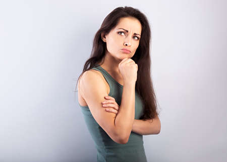 Beautiful serious angry thinking young woman looking up on empty blue studio copy spaceの写真素材