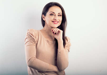 Front view of beautiful thinking woman with natural makeup looking with hand under the face in casual beige blouse on light blue background with empty copy spaceの写真素材