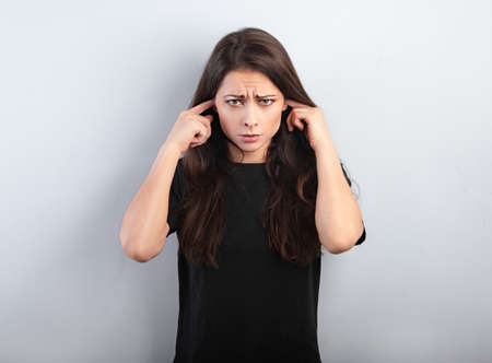 Unhappy stressed grimacing frowns woman not want to listen and covering the ears her fingers on blue background. Closeupの写真素材