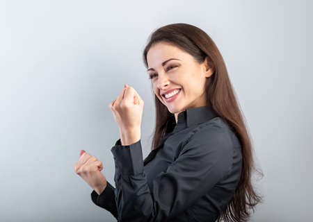 Happy excited business woman showing success triumph sign by fist and loud shouting with open mouth on blue background with empty copy space. Closeup portraitの写真素材