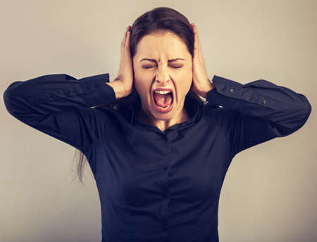 Angry young business woman strong screaming with wild opened mouth and holding the head the hands in...