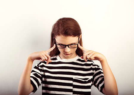 Serious funny kid girl with long hair style in fashion eyeglasses in t-shirt making control physiognomy and looking Closeup toned vintage portraitの写真素材