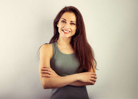 Beautiful casual cute toothy smiling woman hugging your self with folded strong arms in green t-shirt on vintage color background. Closeup toned color portraitの写真素材
