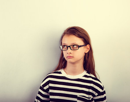 Serious girl with long hair style in fashion eyeglasses in t-shirt making dreaming physiognomy and looking up. Closeup toned vintage portraitの写真素材