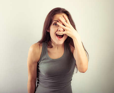 Happy excited surprising beautiful woman with opened mouth covering the face the hands on toned vintage background and happy looking in green sport top. Portraitの写真素材