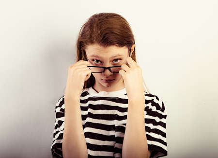 Serious funny kid girl with long hair style in fashion eyeglasses in t-shirt making control physiognomy and looking Closeup toned vintage portraitの写真素材