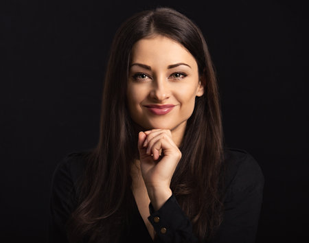 Beautiful confident happy smiling business woman with hand under the face on black background with empty copy space. Closeup portrait of natural happiness. Front center view portraitの写真素材