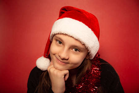 Fun waiting thinking child girl guessing the gift on new year in santa claus hat on red background. Happy Christmas closeup portraitの写真素材