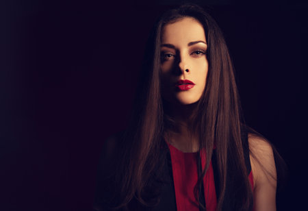 Beautiful bright makeup woman with red lipstick on dark red background with empty copy space. Close up toned portraitの写真素材