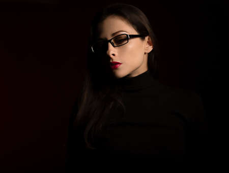 Business thinking woman in fashion eye glasses looking down in black clothing on dark shadow red background. Close up profile view face portraitの写真素材