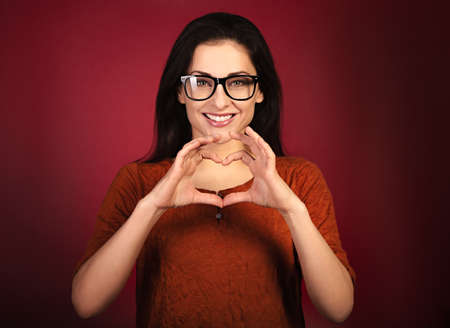 Beautiful healthy woman showing the love heart by two hands with enjoying smiling face on dark red background. close-up portraitの写真素材