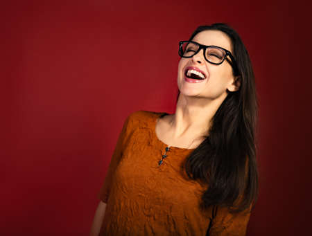 Beautiful toothy laughing happy business woman in good mood in eye glasses and fashion red dress on dark red backround with empty copy space. close-up portraitの写真素材