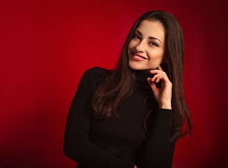 Beautiful tooth confident smiling business woman with red lipstick with hand under the face in black sweater on dark red background with empty copy space. close-up portraitの写真素材