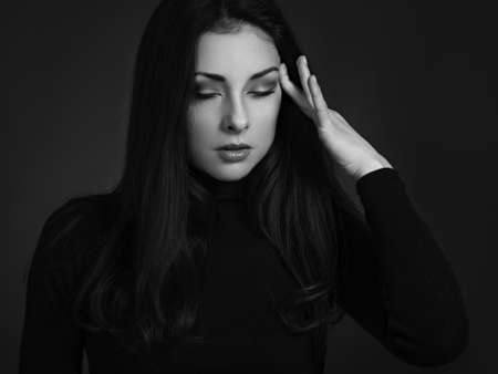 Business concentrate thinking woman find the answer in clever mind with closed eyes with fingers near the face in black sweater on dark shadow red background. closeup. black and whiteの写真素材