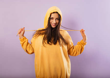 Relaxing toothy smiling sporty woman posing in fashion yellow hoodie on purple bright background with empty copy space. happy portraitの写真素材