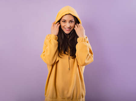 Relaxing toothy smiling sporty woman posing in fashion yellow hoodie on purple bright background with empty copy space. happy portraitの写真素材
