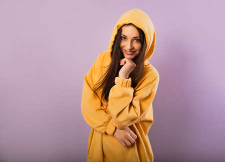 Relaxing thinking smiling sporty woman posing in fashion yellow hoodie with hood on the head on...