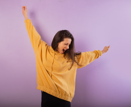 Fun enjoying active smiling sporty woman posing in fashion yellow hoodie on purple bright background with empty copy space. happy studio portraitの写真素材