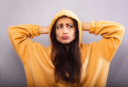 Fun grimacing confused woman posing in fashion yellow hoodie looking unhappy in hood on the head on...