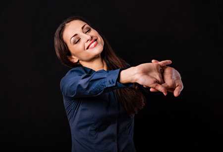 Beautiful happy smiling business woman relaxing and doing stretching exercise on shoulder blades pulling the parms isolated on black background with empty copy space. Closeupの写真素材