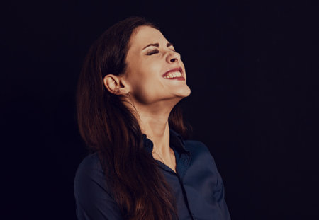 Beautiful funny toothy laughing business woman with folded arms in blue shirt on black background with empty copy space for text. Closeup vintage toned portraitの写真素材