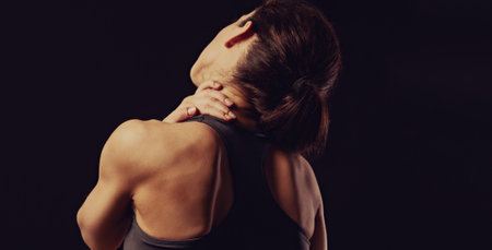 Sporty woman doing hand the massage to relax the tension in shoulder and neck in sport bra top on empty copy space black studio background. Closeup back view. The concept of medicine. Toned colorの写真素材