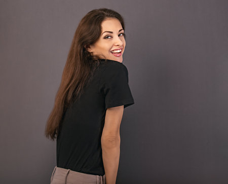Beautiful positive laughing business happy woman in black t-shirt looking in camera on empty copy space gray background. close-up portraitの写真素材