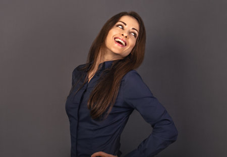 Beautiful positive business happy woman in blue shirt looking back with toothy smile on empty copy space gray background. close-up portraitの写真素材