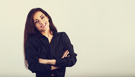 Happy toothy enjoying smiling woman posing in black shirt standing with folded arms on toned vintage background with empty copy space. Closeup front classic banner portraitの写真素材