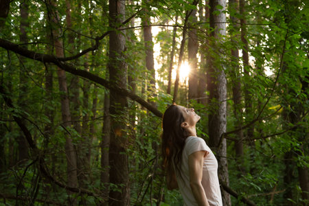 Beauty woman smiling sun summer light in a pine forest. Female relaxing and enjoying in a park in good weather. Girl breath deep in green woodsの写真素材