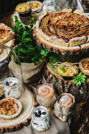 Pear pie, cupcakes and cinnabbons on wooden stumps, near a green plantの写真素材
