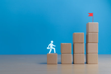 Self development and growth. Businessman climbs the stairs to the red flag to achieve his final goalの写真素材