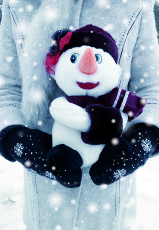 woman's hands in mittens holding snowman toy with snow and snowflakesの写真素材