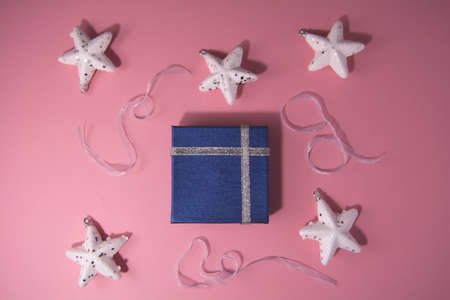 Holiday concept. Beautiful blue gift with silver ribbon and white shiny stars, ribbon on pink backgroundの写真素材