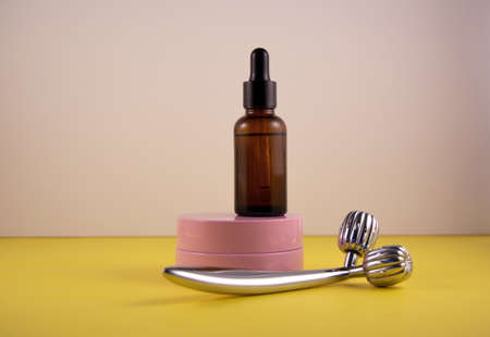 The concept of facial care and the fight against age-related changes. Metal roller, pink jar of cream and bottle of serum. Front veiw.の写真素材
