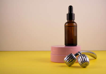 The concept of facial care and the fight against age-related changes. Metal roller, pink jar of cream and bottle of serum. Front veiw. Copy space.の写真素材