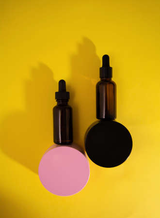 Cosmetic containers jar of cream and bottle of serum on yellow background. Flat lay, top view and copy spaceの写真素材