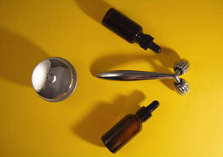 Modern selfcare concept and anti-age care. Face metal roller and serum on yellow background. Top view and flat lay.の写真素材