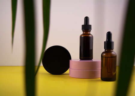 Beauty product concept. Jar of cream and bottle of serum on yellow and white backgrounds. Green...
