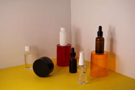 Beauty product concept. Cosmetic containers on the orange and red transparent podium. Front view, copy spaceの写真素材