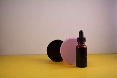 Beauty product concept. Jar of cream and bottle of serum on yellow and white backgrounds. Front view, copy spaceの写真素材