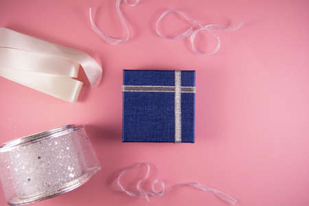 Preparation for holidays. White and silver ribbons and blue gift for the holiday on pink background. Top view and copy spaceの写真素材