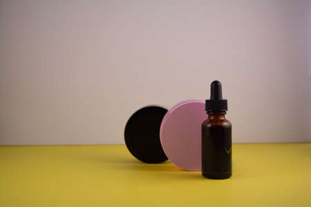 Beauty product concept. Jar of cream and bottle of serum on yellow and white backgrounds. Front view, copy spaceの写真素材