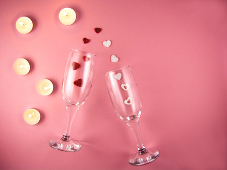 Two glasses with splash of red and white heart and burning candles on a pink background.の写真素材