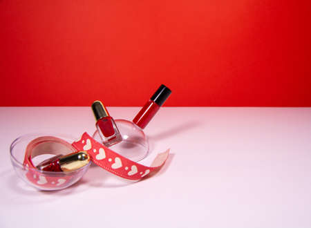 Red lipstick and nail polish on white table with red backgroundの写真素材