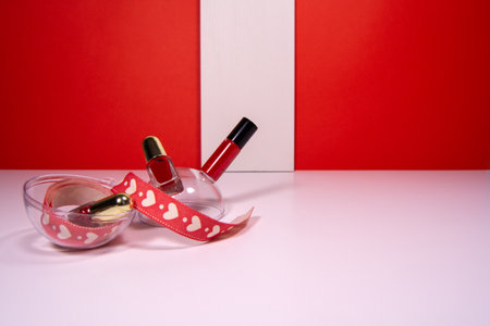 Red lipstick and nail polish on white table with white stripe on red backgroundの写真素材