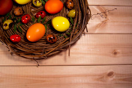 Eggs painted yellow, orange and brown lie in a nest made of wooden twigs on wooden table. The eggs lie with green twigs. Easter and spring concept. Copy space and top viewの写真素材